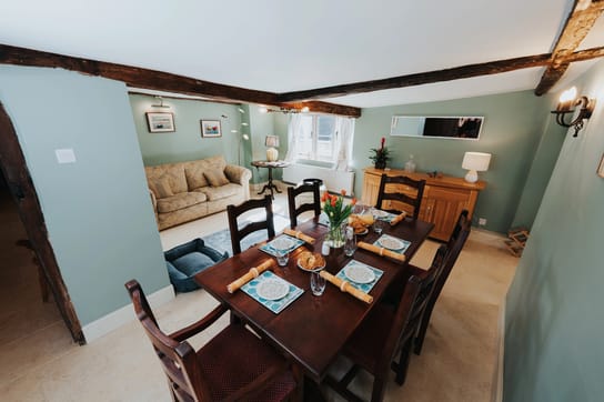Notehouse Farms dining area with pale green walls, exposed wooden beams, a set dining table, and a cosy sitting area by the window