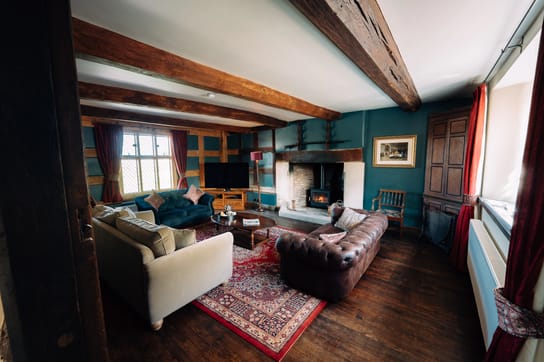 Living room at Notehouse Farms with exposed timber beams, comfortable sofas, a patterned rug, and a lit fireplace.