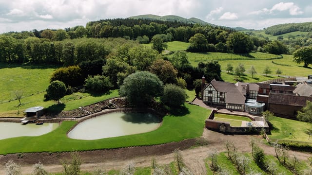 Farmhouse with ponds and landscaped grounds surrounded by fields and wooded hills