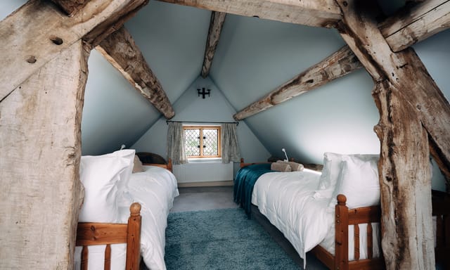 Twin bedroom at Notehouse Farms with exposed timber beams, white bedding, and a pitched ceiling.
